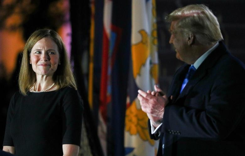 Judge Amy Coney Barrett looks over at President Trump as he stands behind a teleprompter before Barrett is sworn in to serve as an associate justice of the U.S. Supreme Court on the South Lawn of the White House in Washington.   REUTERS/Tom Brenner  